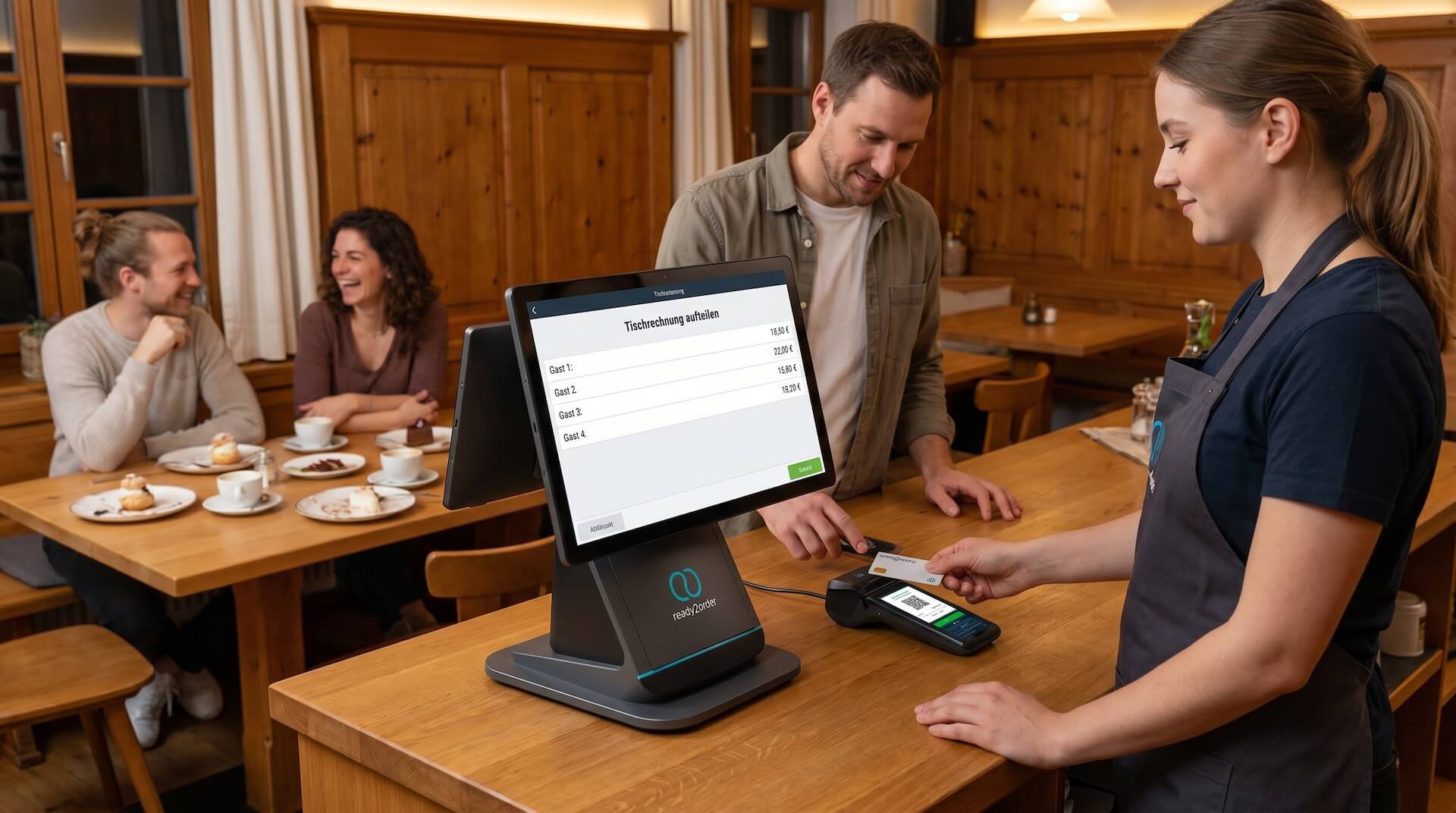 Servicekraft bedient ein ready2order Kassenterminal, auf dem Display ist die Maske „Tischrechnung aufteilen" mit Einzelbeträgen für Gast 1 bis Gast 4 geöffnet. Ein Gast hält daneben eine Karte an das Kartenterminal, im Hintergrund sitzen zwei weitere Gäste am Tisch.
